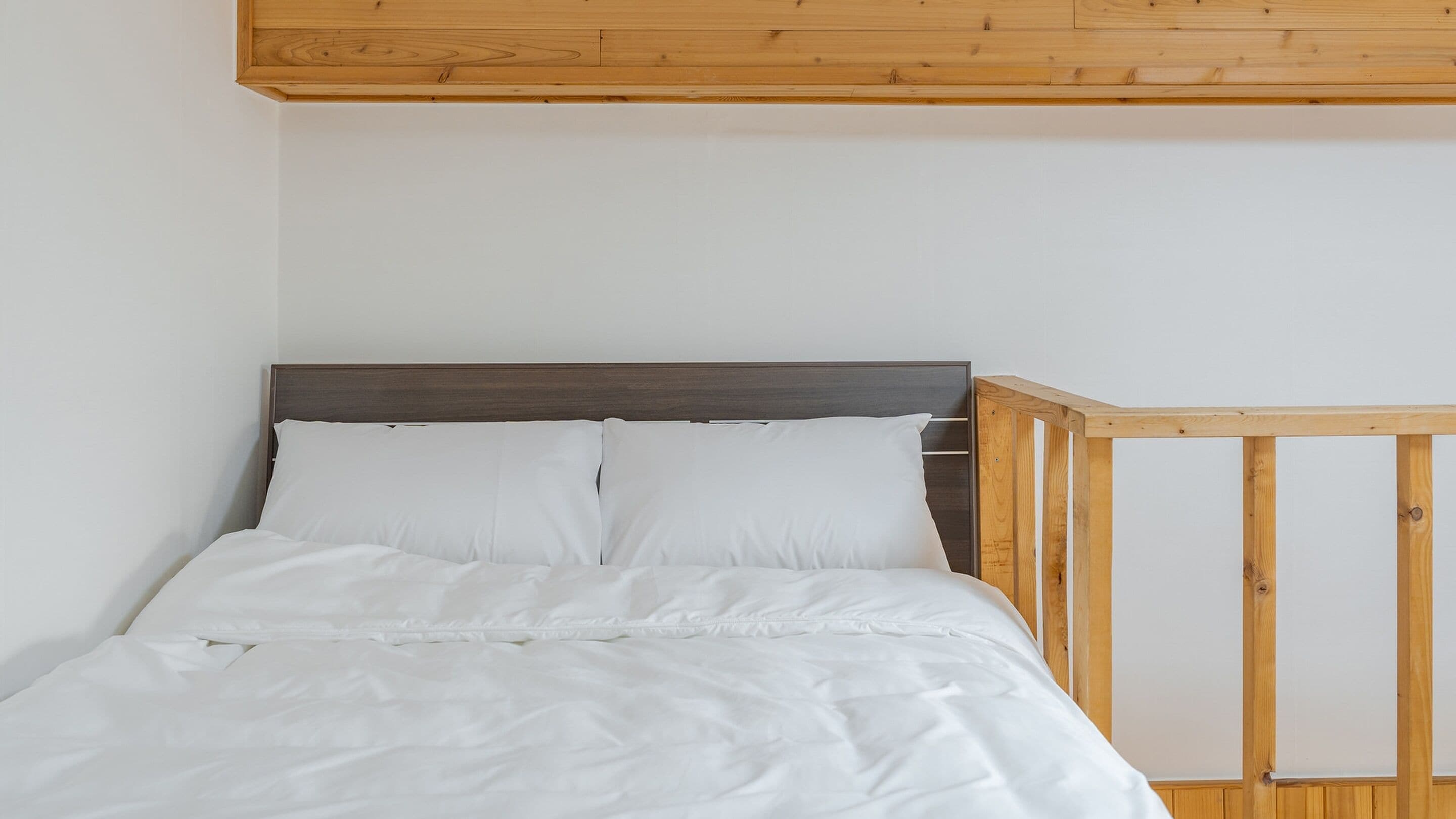 Una cama con ropa blanca, cabecera de madera y una cuna de madera a la derecha.