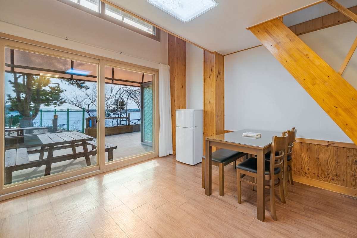 A modern kitchen with wooden accents, a dining area with a table and chairs, and a view of a balcony with outdoor furniture.