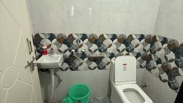 A bathroom with a toilet, sink, and shower. There is a green bucket on the floor.