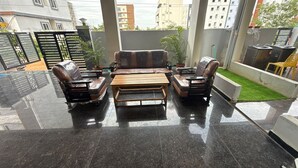 A modern outdoor seating area with a sofa and two armchairs, a wooden coffee table, and a small patch of artificial grass. - COCO NET Hotel (Ibrahimpatan)