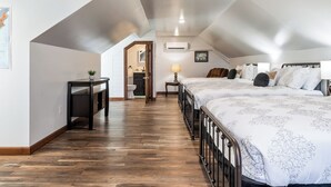 Een slaapkamer met een houten vloer, een bed met beddengoed met een patroon, een bureau met een plant, en een zichtbare badkamer door een geopende deur.
