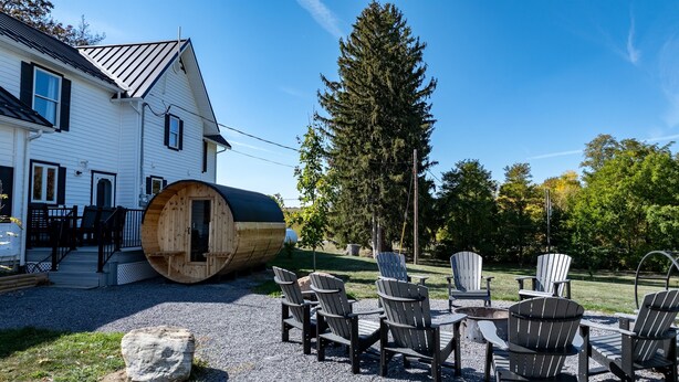 Een huis met een groot houten vat, buiten zitplaatsen en een bos op de achtergrond.