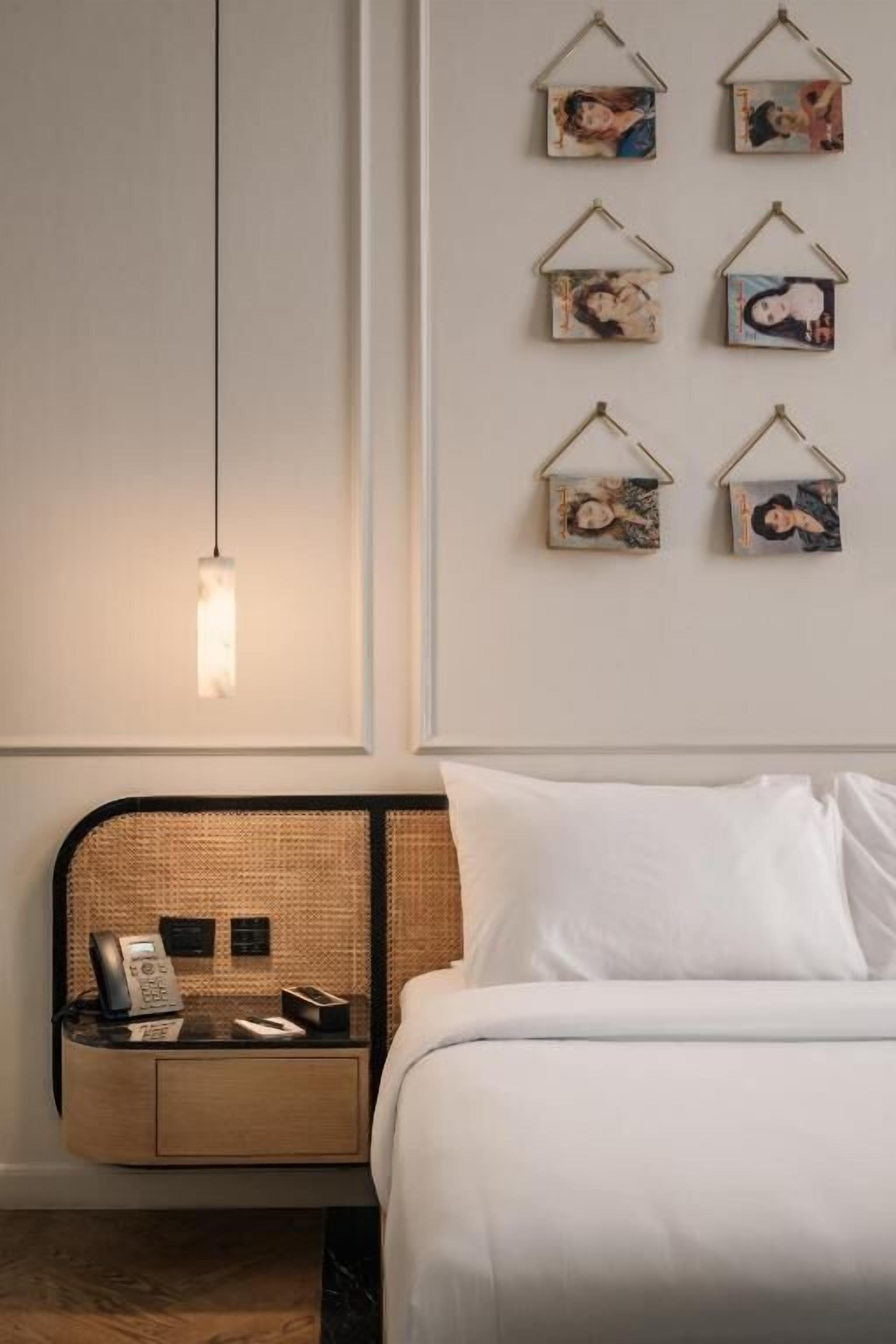 Una habitación de hotel con una cama, una mesita de noche con un teléfono y una lámpara, y una pared con cuadros.