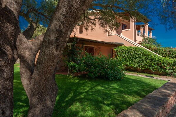 Une maison avec un chemin de pierre menant à l’entrée, entourée d’une végétation luxuriante et d’arbres.