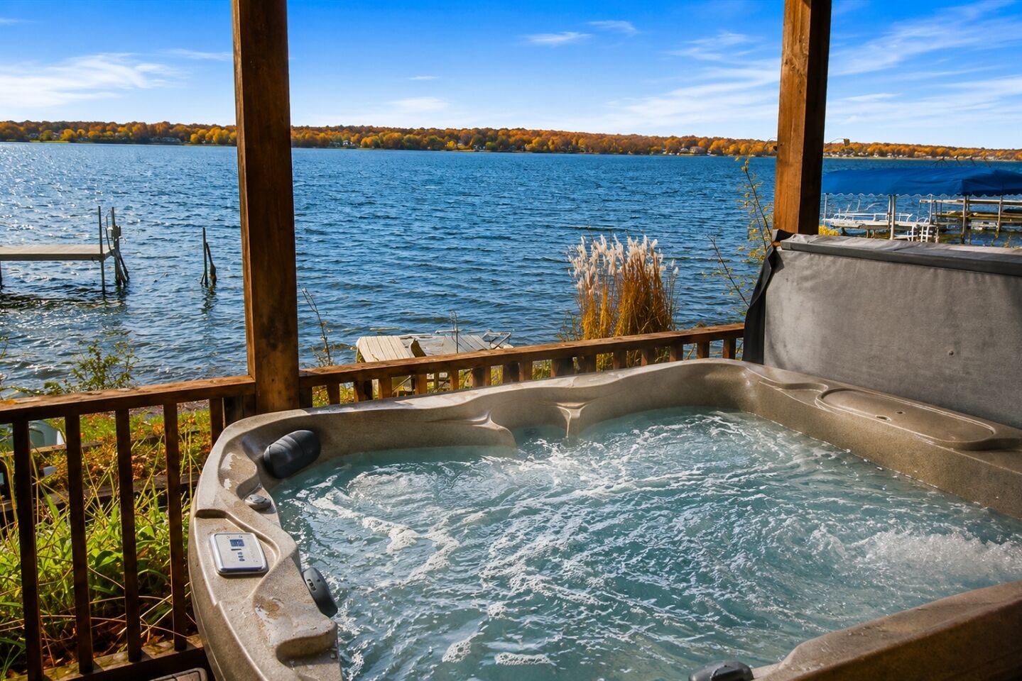 A hot tub with a wooden deck and a view of a lake and trees.