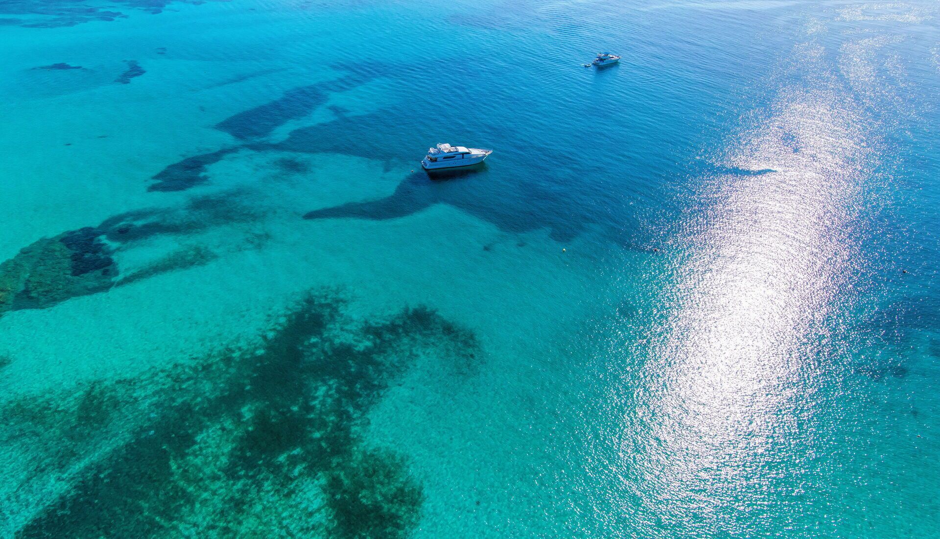 An aerial view of a clear turquoise sea with a boat anchored near the shore.