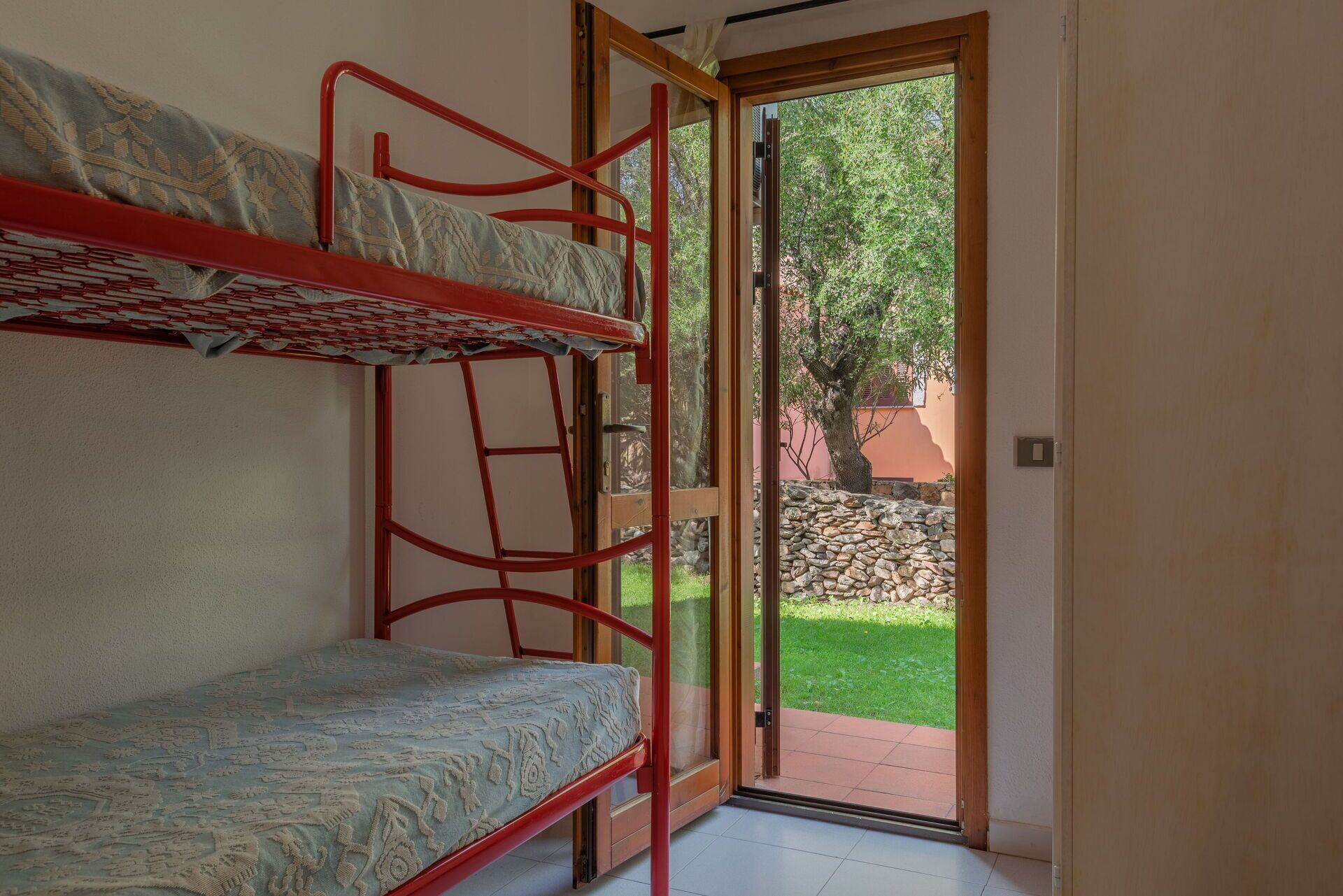 Una camera con letto a castello e una porta in vetro che dà su una zona esterna con un muro in pietra e un albero.