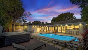 Un jardin avec une piscine, des chaises longues, un jacuzzi et un patio couvert.