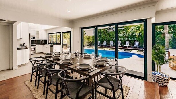 Un espace repas moderne avec vue sur la piscine, une cuisine et une grande porte-fenêtre coulissante.