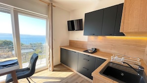 A modern kitchen with black cabinets, a wooden countertop, and a view of the sea. - Studio Apartman Kira 5 (Dramalj)