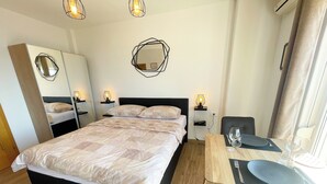 A bedroom with a bed, bedside tables, a mirror, a desk with a chair, and a window with curtains. - Studio Apartman Kira 5 (Dramalj)