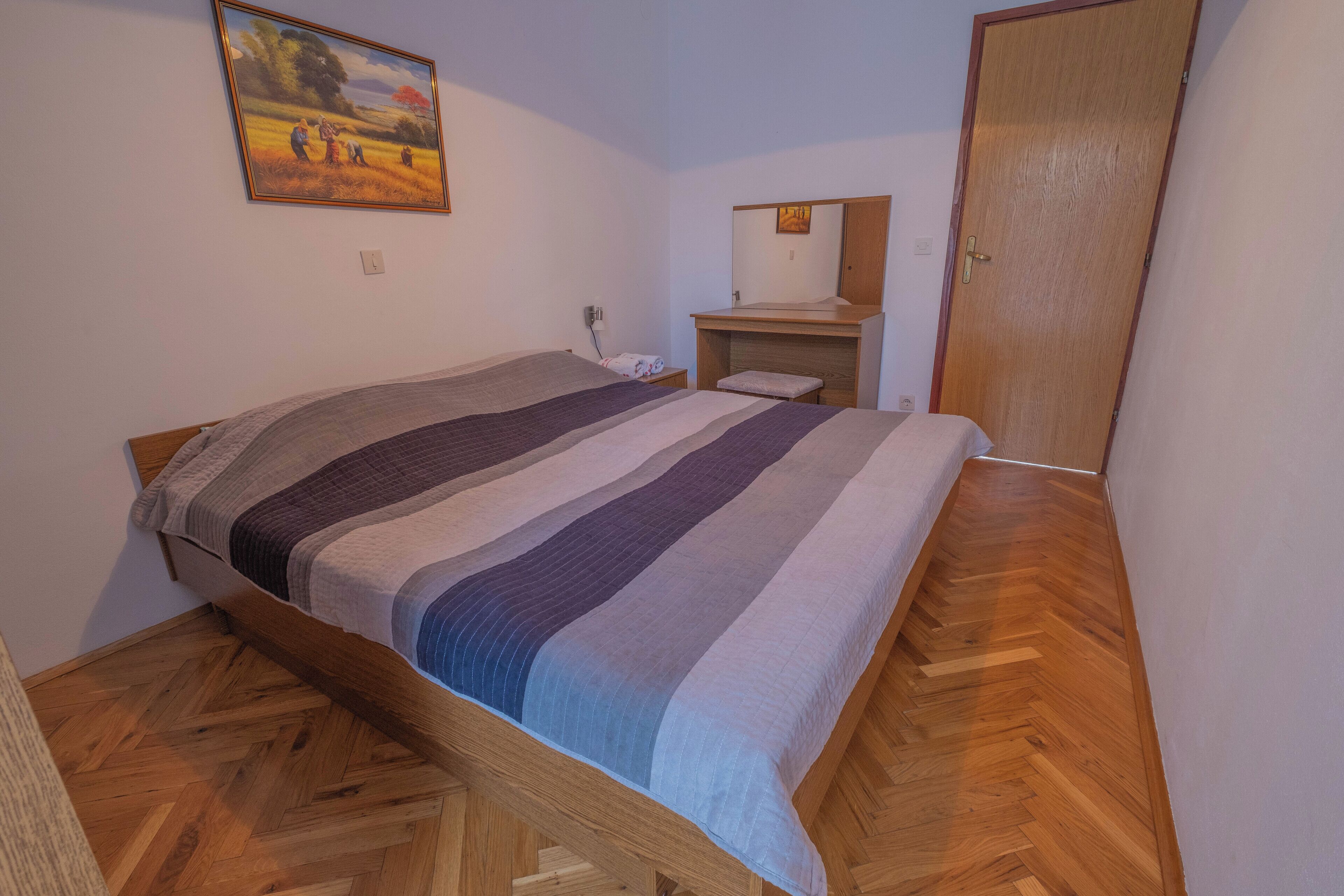 Ein Schlafzimmer mit einem hölzernen Bett, einem Nachttisch, einem Spiegel und einer Tür.