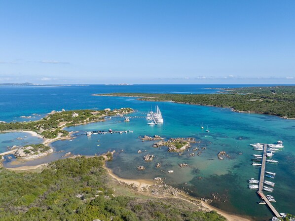 An aerial view of a coastal area with clear turquoise waters, a marina with several boats, and a small island with buildings and greenery. - Cosy apartment for 4 people with A/C, WIFI, TV and panoramic view, close to Olbia (Golfo Aranci)