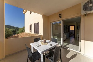 A balcony with a table and chairs, a sliding glass door to a living area, and a view of a hillside. - Cosy apartment for 4 people with A/C, WIFI, TV and panoramic view, close to Olbia (Golfo Aranci)