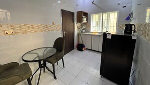 Eine kompakte Küche mit weißen Fliesen, einem kleinen Esstisch mit Stühlen, einem Kühlschrank und einem Fenster mit Blick.