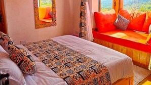 A bedroom with a large bed, a window seat with orange cushions, and a view of the outdoors. - ol eburru cottage naivasha (Naivasha)