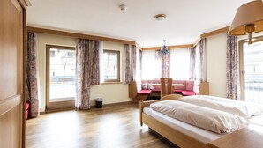 A hotel room with a wooden bed, a pink sofa, a small table, and a window with curtains. - Heart Hotel Nordstern (Mayrhofen)