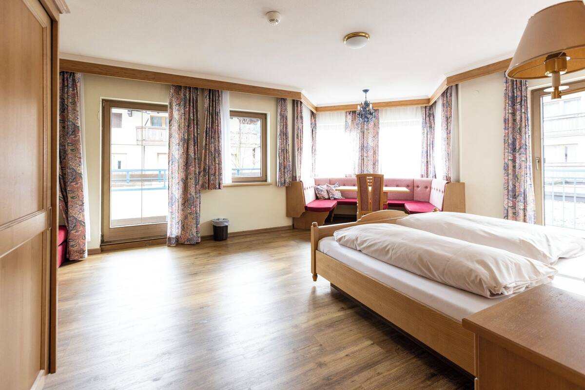 Habitació d'hotel amb un llit de fusta, un sofà rosa, una taula petita i una finestra amb cortines.