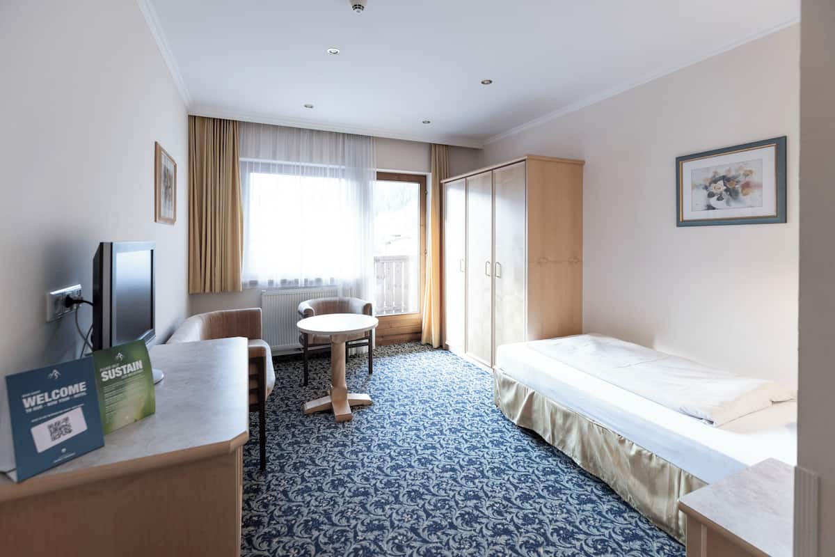 Habitació d'hotel amb un llit, escriptori, cadira, taula petita, televisió i finestra amb cortines.