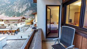 A balcony with a view of a mountain, a dining area with people, and a room with a bed and a TV. - Heart Hotel Nordstern (Mayrhofen)