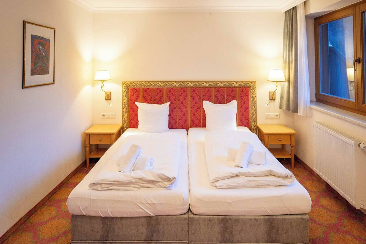 Habitació d'hotel amb dos llits, un mosaic de moqueta, un llum decoratiu al sostre i una finestra amb cortines.