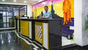 A reception desk with a person seated behind it, a large mural of a figure in traditional attire, and a modern interior design with a marble floor. - HOTEL STAAR WORLD (Nagercoil)
