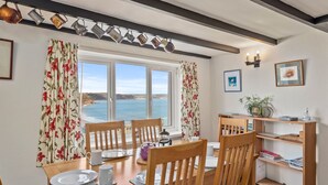 Un'area pranzo con un tavolo e sedie in legno, una finestra vista mare e una libreria con libri e oggetti decorativi.