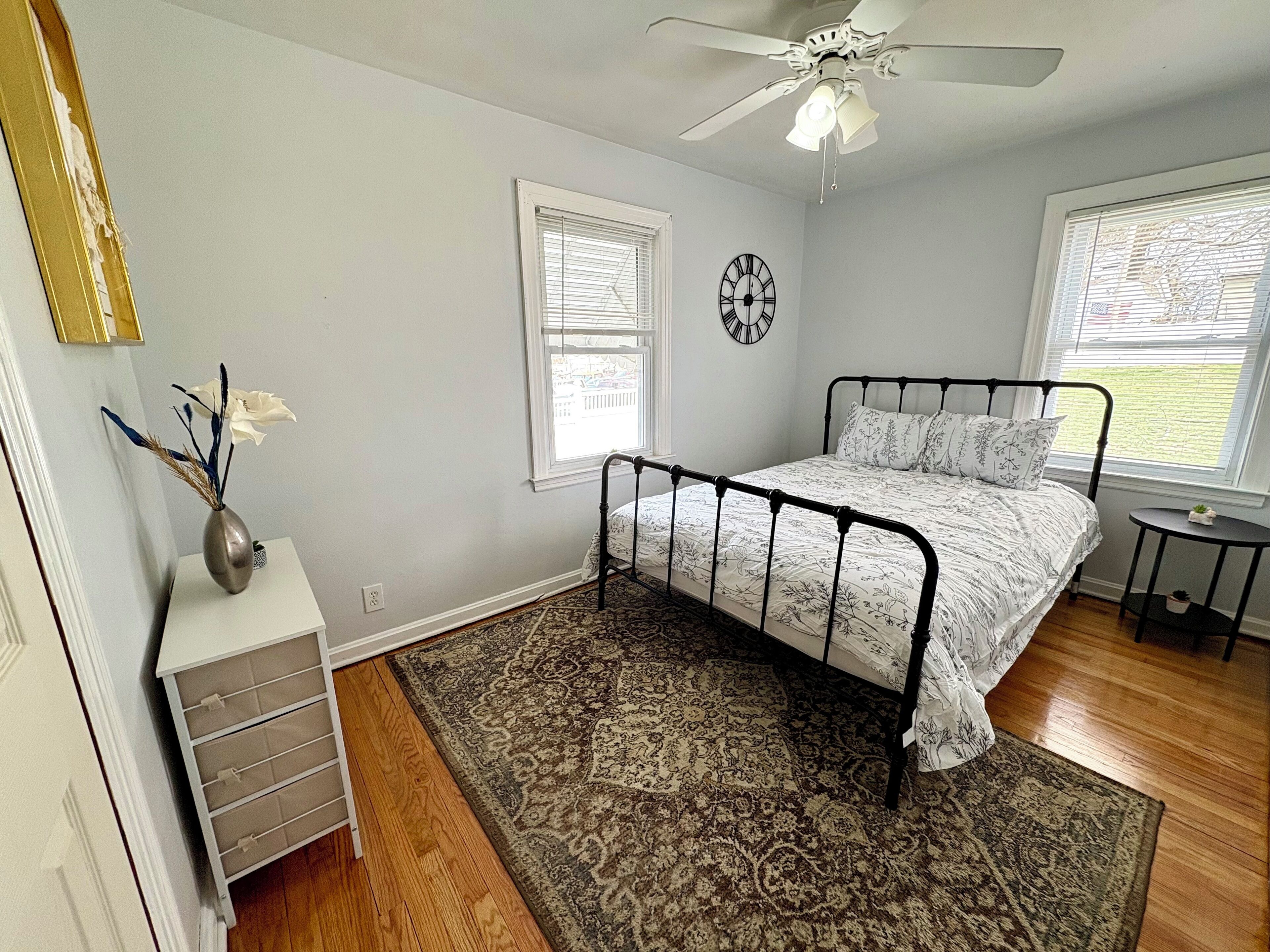 A bedroom with a bed, a ceiling fan, a clock, and a window.