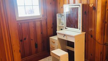 Une petite pièce aux murs lambrissés, comprenant un bureau, une chaise, une fenêtre et un tapis blanc.