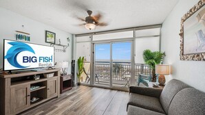 Un salón amplio con televisor grande, muebles de madera, ventilador de techo y balcón con vistas.