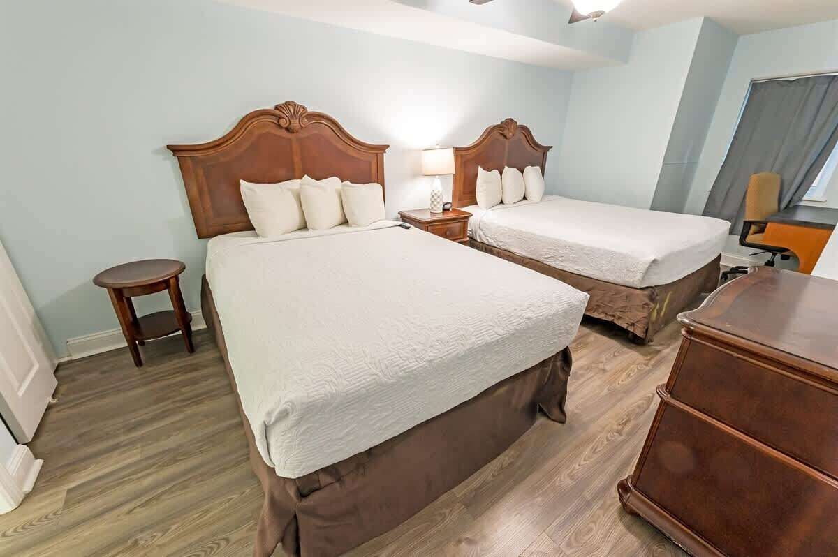 A hotel room with two beds, wooden headboards, a small round table, and a dresser.