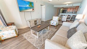 Ein Wohnzimmer mit einer Couch, Sesseln, einem Couchtisch und einem an der Wand befestigten Fernseher.