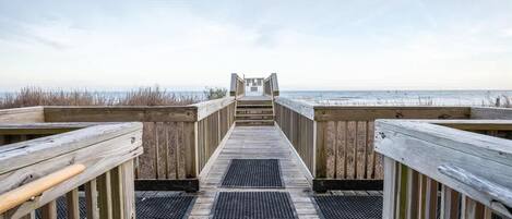 En träpromenad som leder till en strand med fri utsikt över havet.