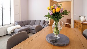 Un salón con una mesa de comedor de madera, un sofá gris y un jarrón con flores.