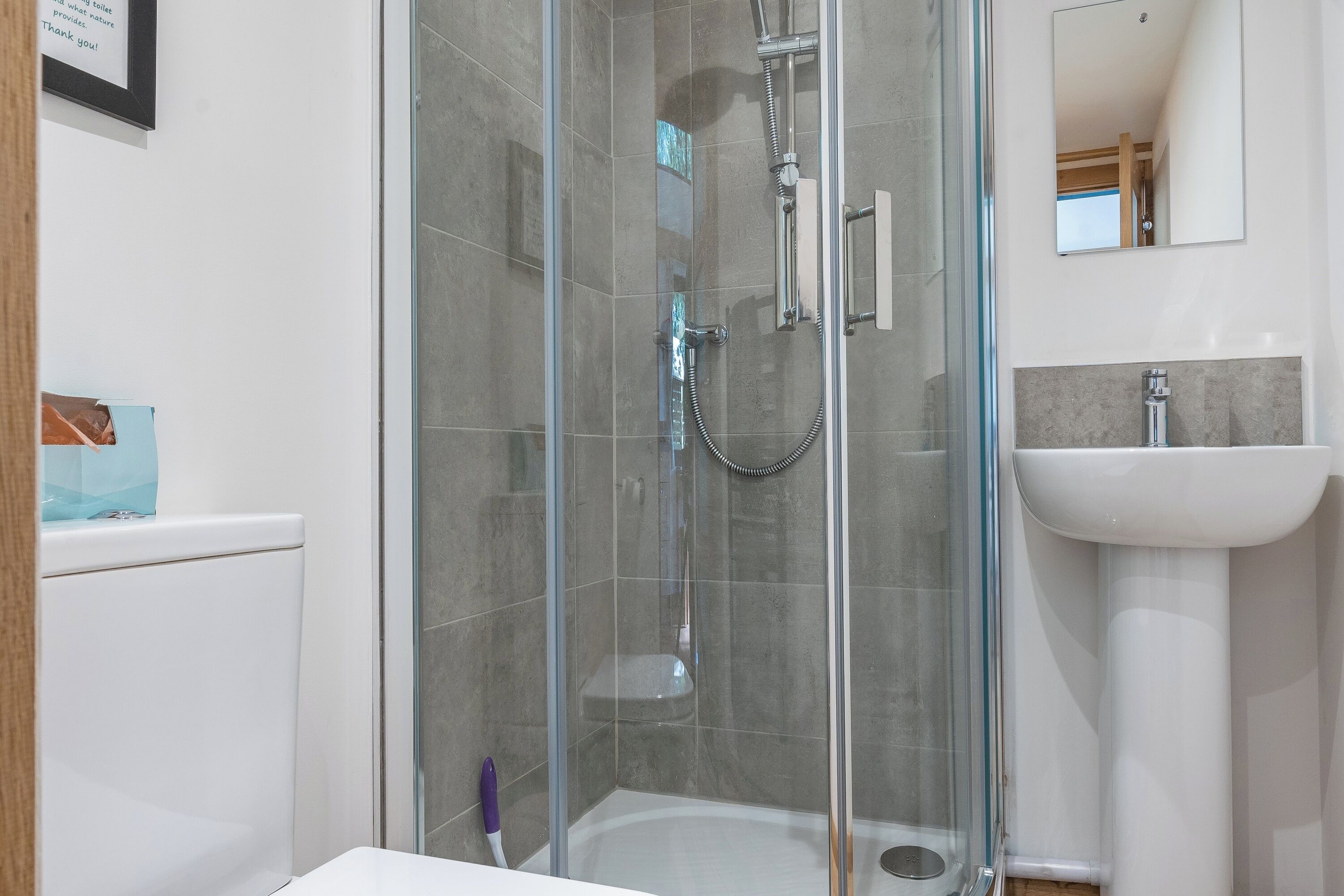 A modern bathroom with a glass-enclosed shower, a white sink, and a framed sign on the wall.