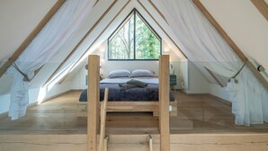Ein Schlafzimmer mit großem Fenster, Holzbalken und einem Bett mit Kissen.