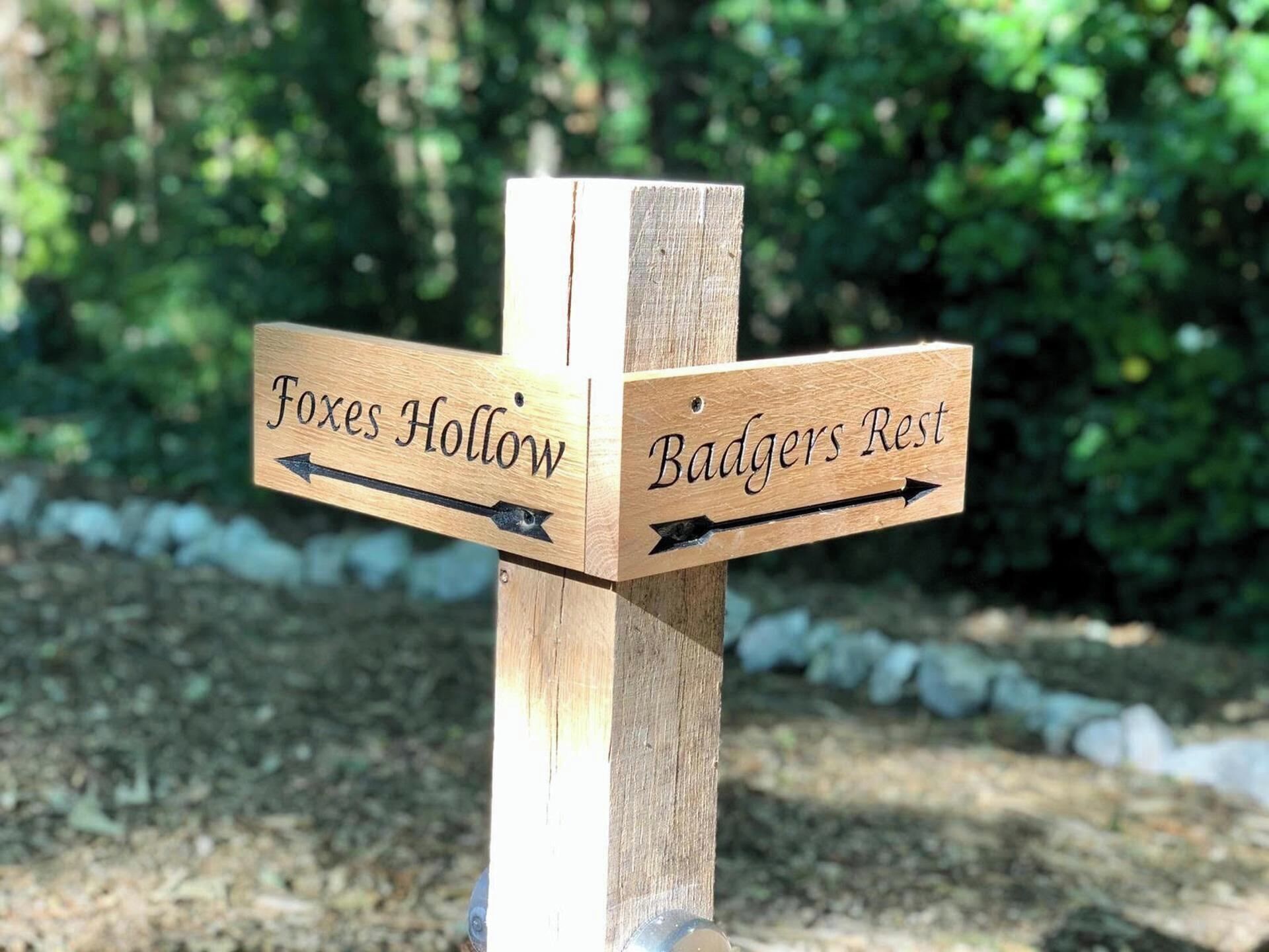 Un panneau de signalisation en bois, avec des flèches indiquant la direction de « Foxes Hollow » et de « Badgers Rest ».