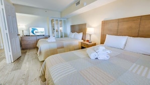 Habitación de hotel con dos camas, televisión, armario y baño visible a través de una puerta.