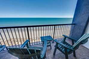 A balcony with a view of the beach, featuring two green chairs and a small table. - NEW Upscale1BR Direct Oceanfront View,King,Pools (Myrtle Beach)