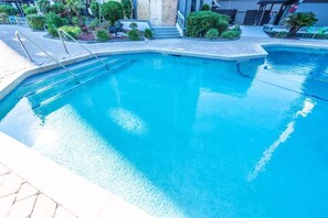 Piscina com degraus para acesso, rodeada por vegetação e um edifício ao fundo.