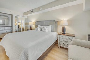 Quarto de hotel bem arrumado com uma cama grande, cômoda, cadeira e espelho.