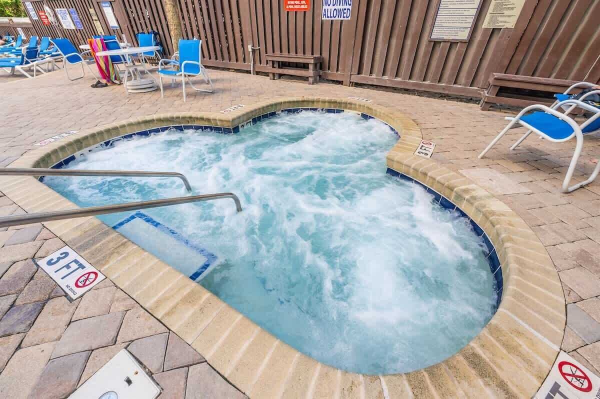 A hot tub with a wooden deck and blue chairs.