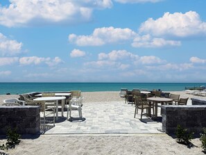 Een terras aan het strand met buitenmeubels en uitzicht op de oceaan.