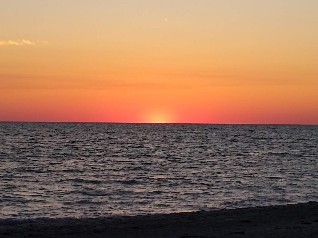 A sunset over a calm sea with a beach in the foreground.