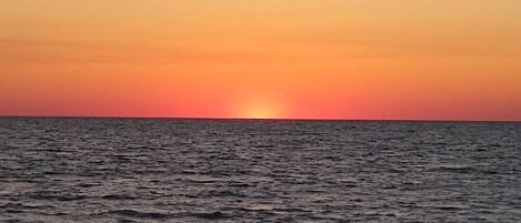 A sunset over a calm sea with a beach in the foreground.