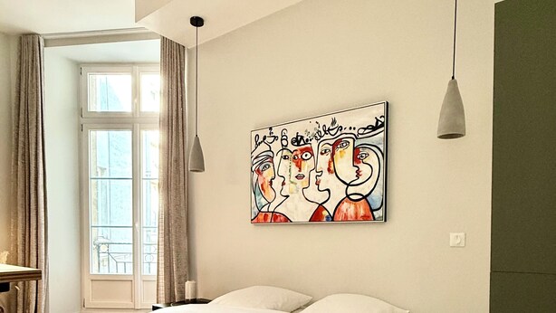 A bedroom with a large bed, a green blanket, a white rug, a painting on the wall, and a window with curtains. - Id-home Le Saint Nicolas (Nantes)