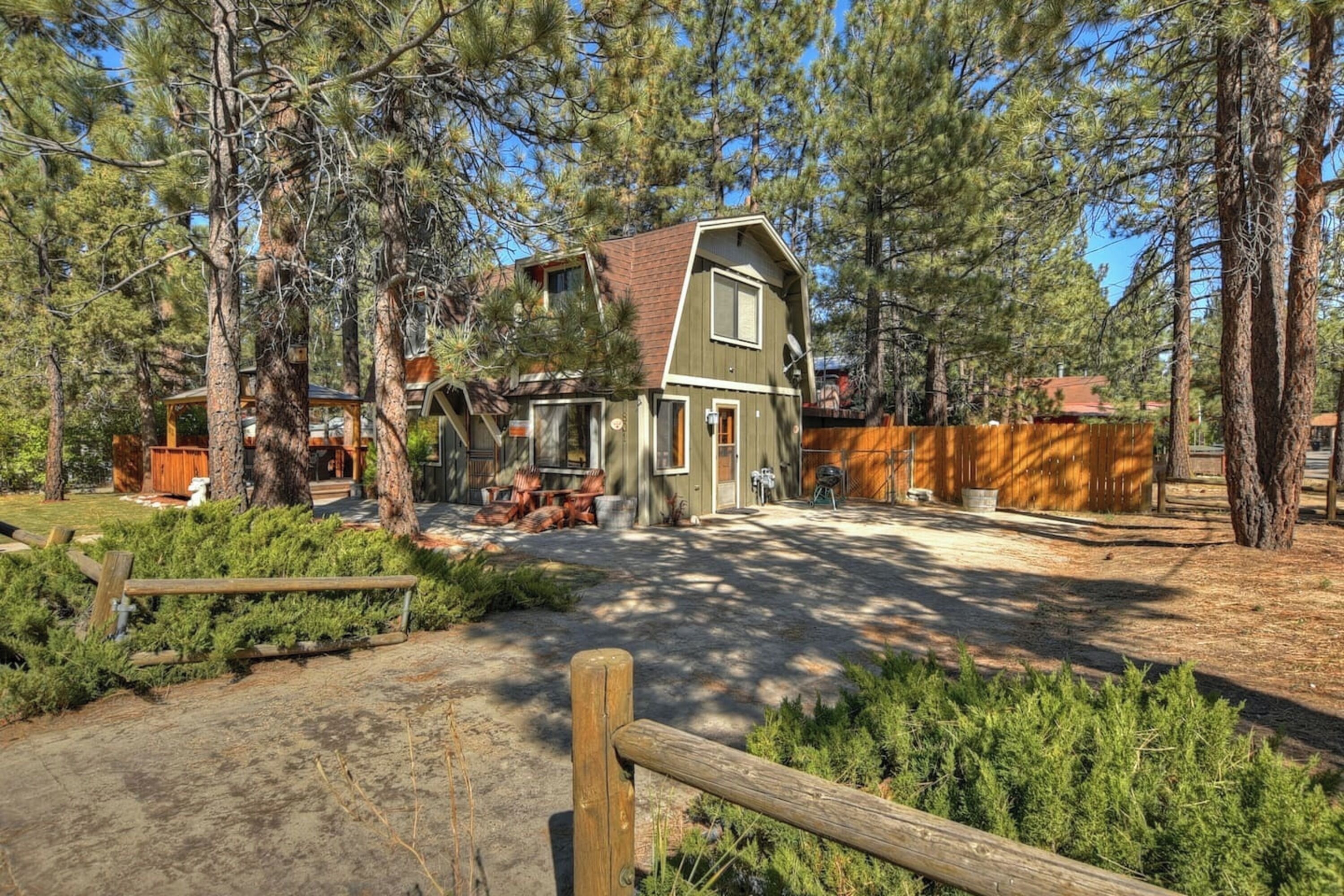 A two-story house with a sloped roof, surrounded by tall pine trees.