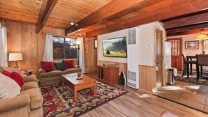 Ein gemütliches Wohnzimmer mit Holzwänden und -decken, einer Sofagarnitur, einem Couchtisch und einem Fernseher.