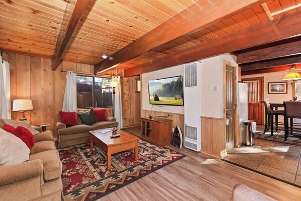 Una sala de estar acogedora con paredes y techo de madera, un conjunto de sofás, una mesa de centro y un televisor.