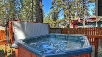 A hot tub outdoors with a wooden deck and trees in the background.
